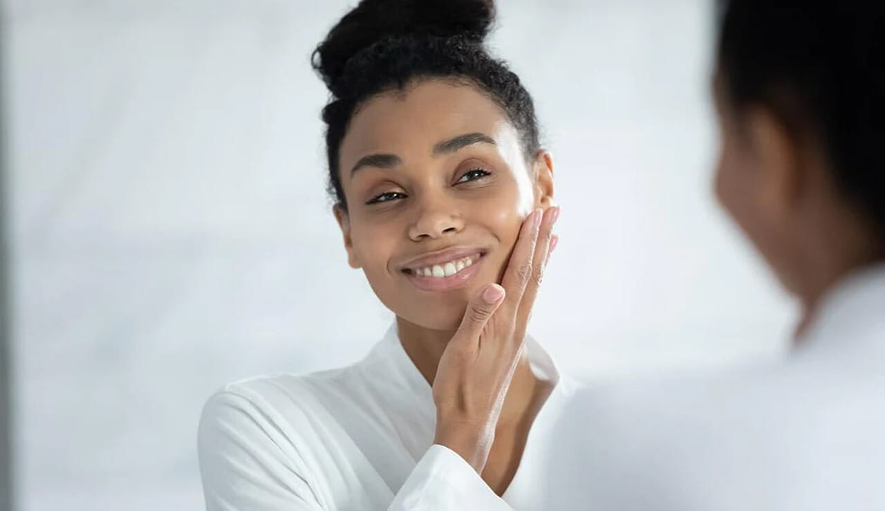 Mulher passando mão no rosto sorrindo para um espelho