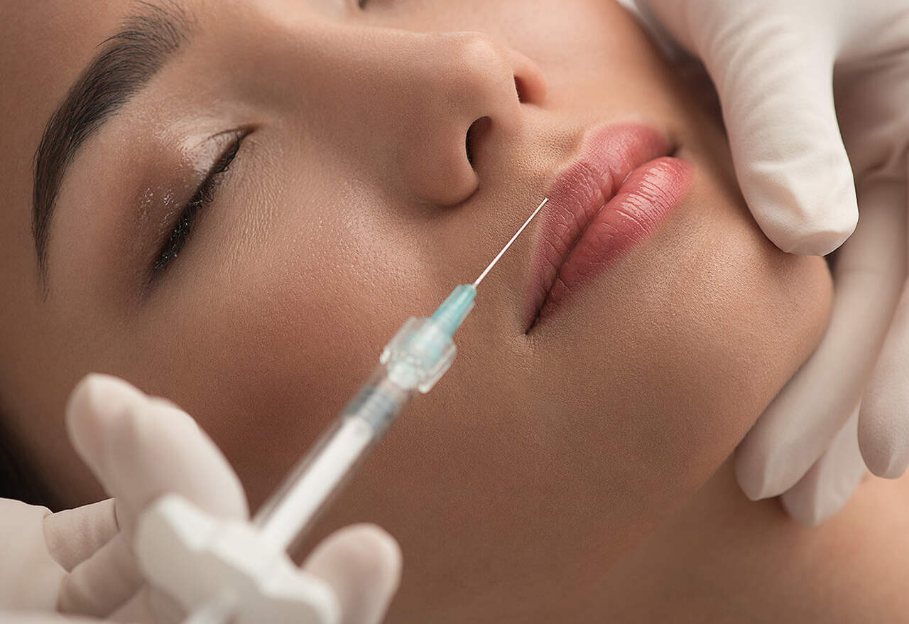 profissional com seringa fazendo harmonização facial com mulher de olhos fechados.